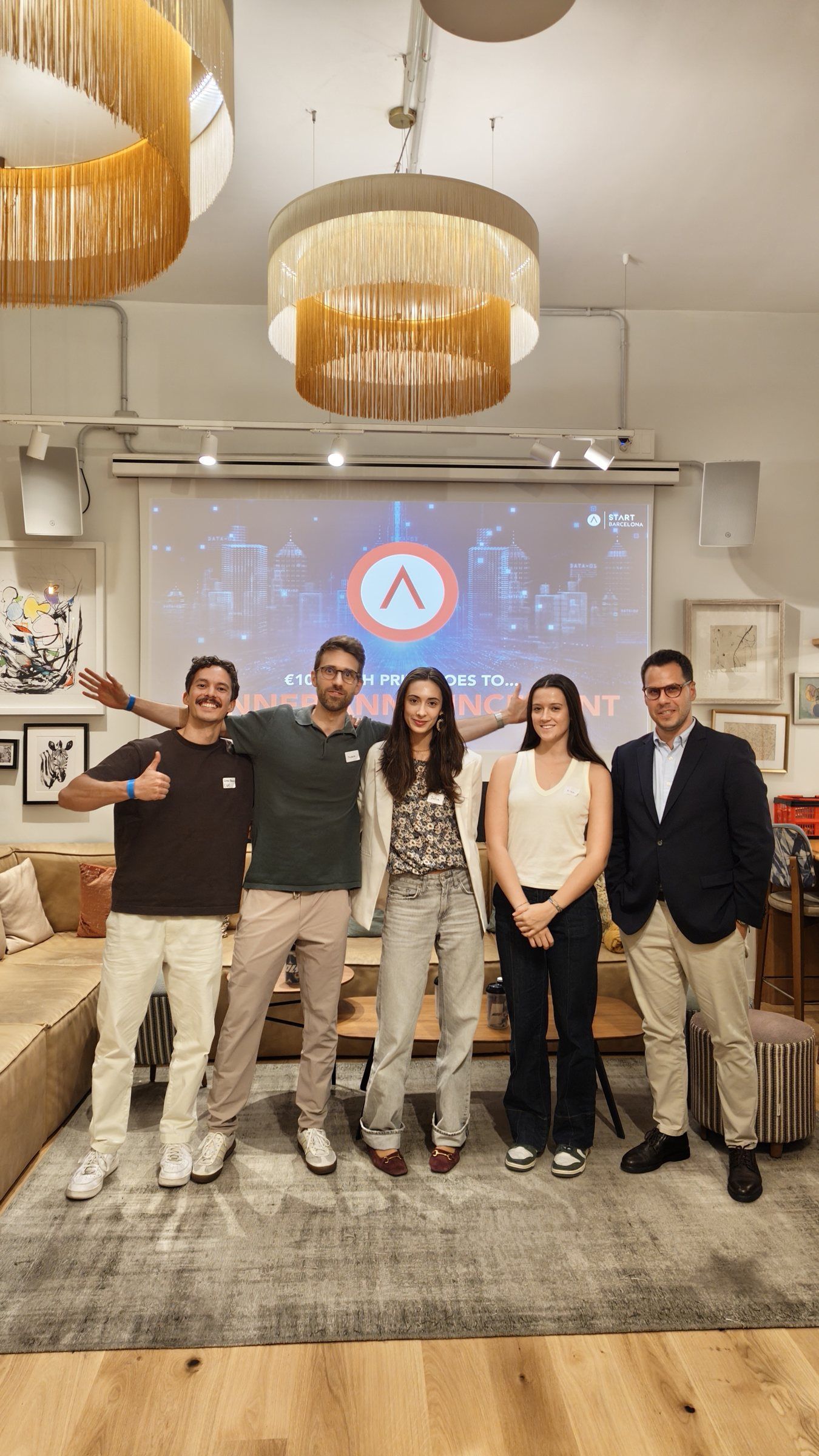 The winning team posing with the organisers in front of the screen, one giving a thumbs up