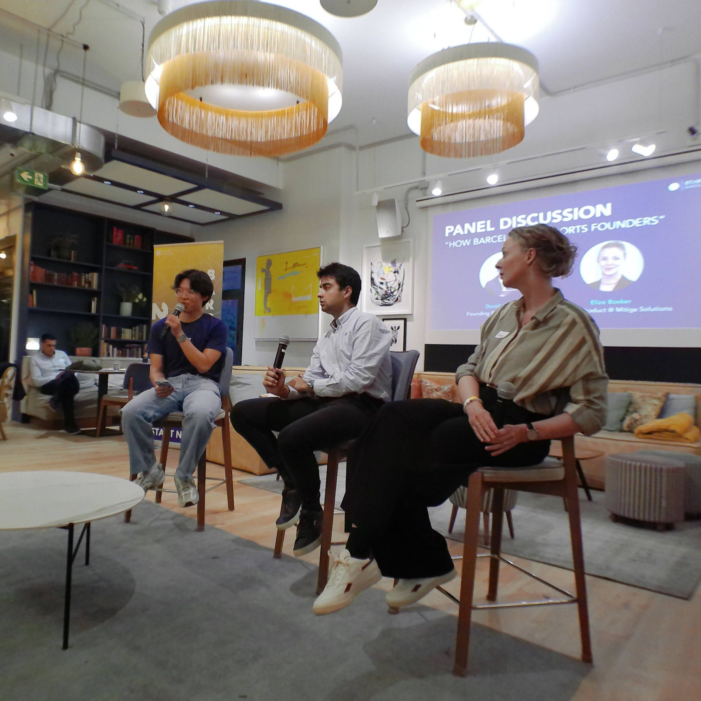 Digicam photo of the LaunchLab panel, three speakers on high stools in front of the slide