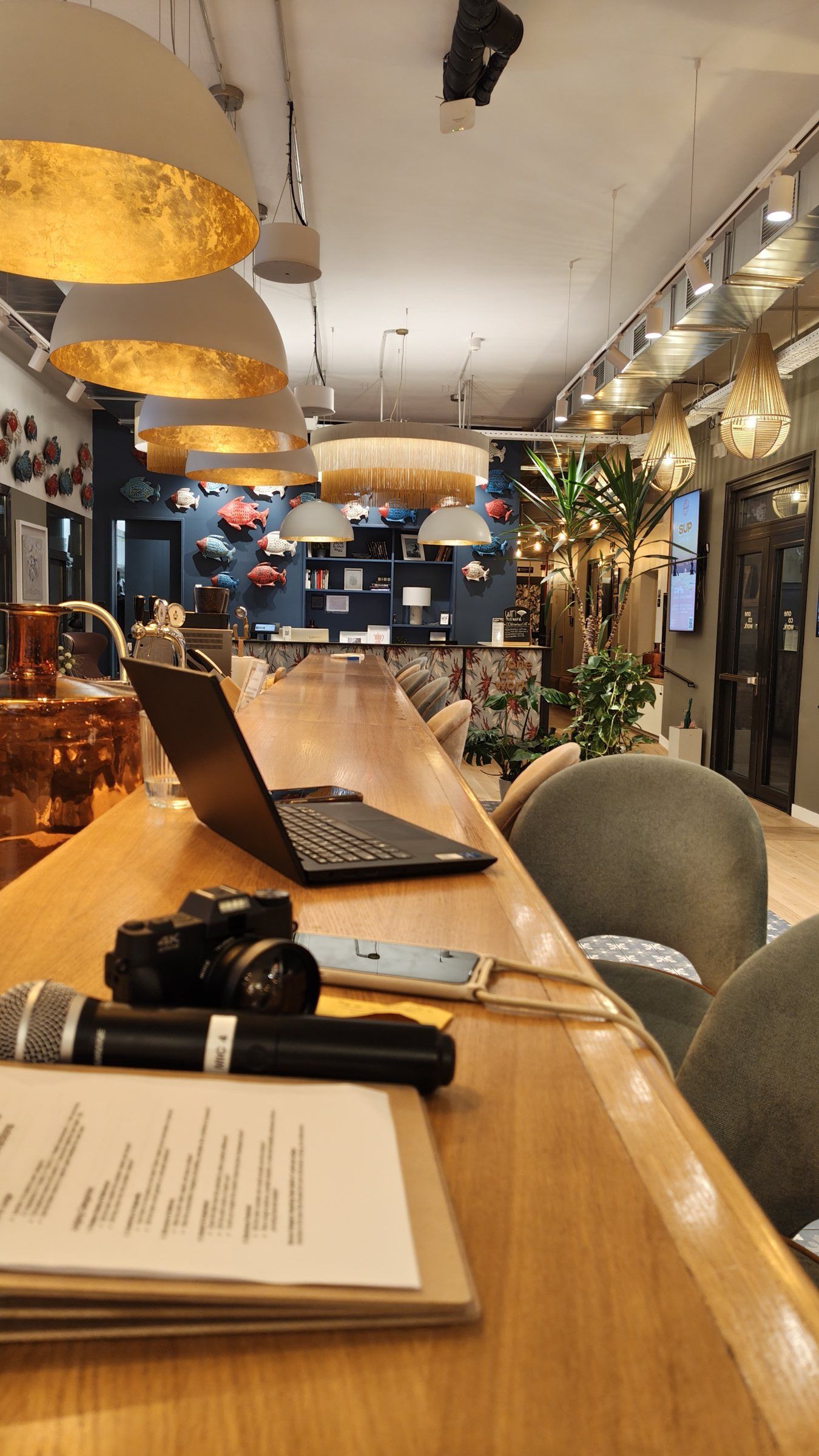 A laptop, a camera, a microphone and printed run sheets on a wooden table