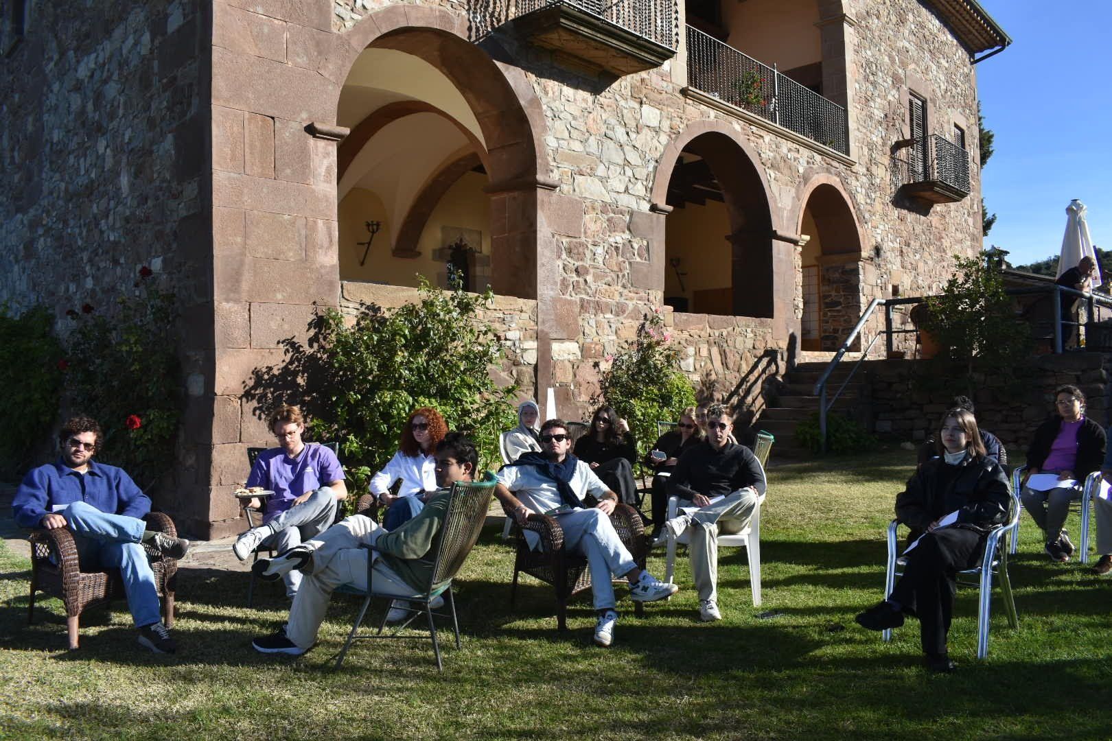Members sitting in garden chairs on the lawn in front of an old stone house