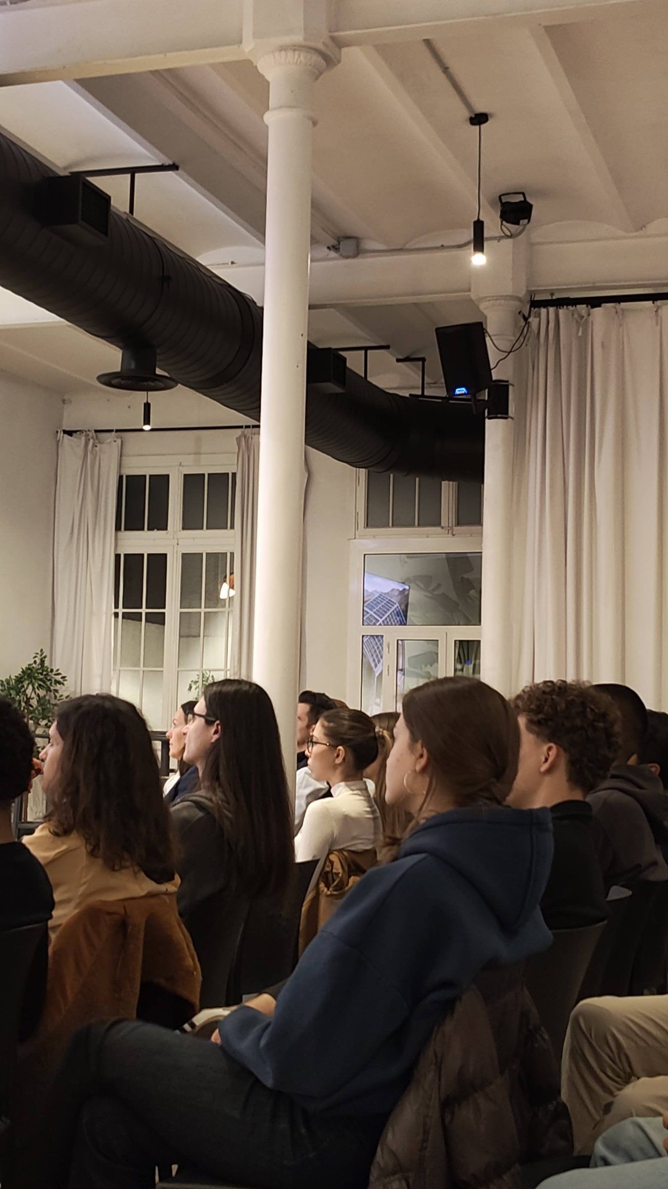 The audience seated between white columns, watching the stage