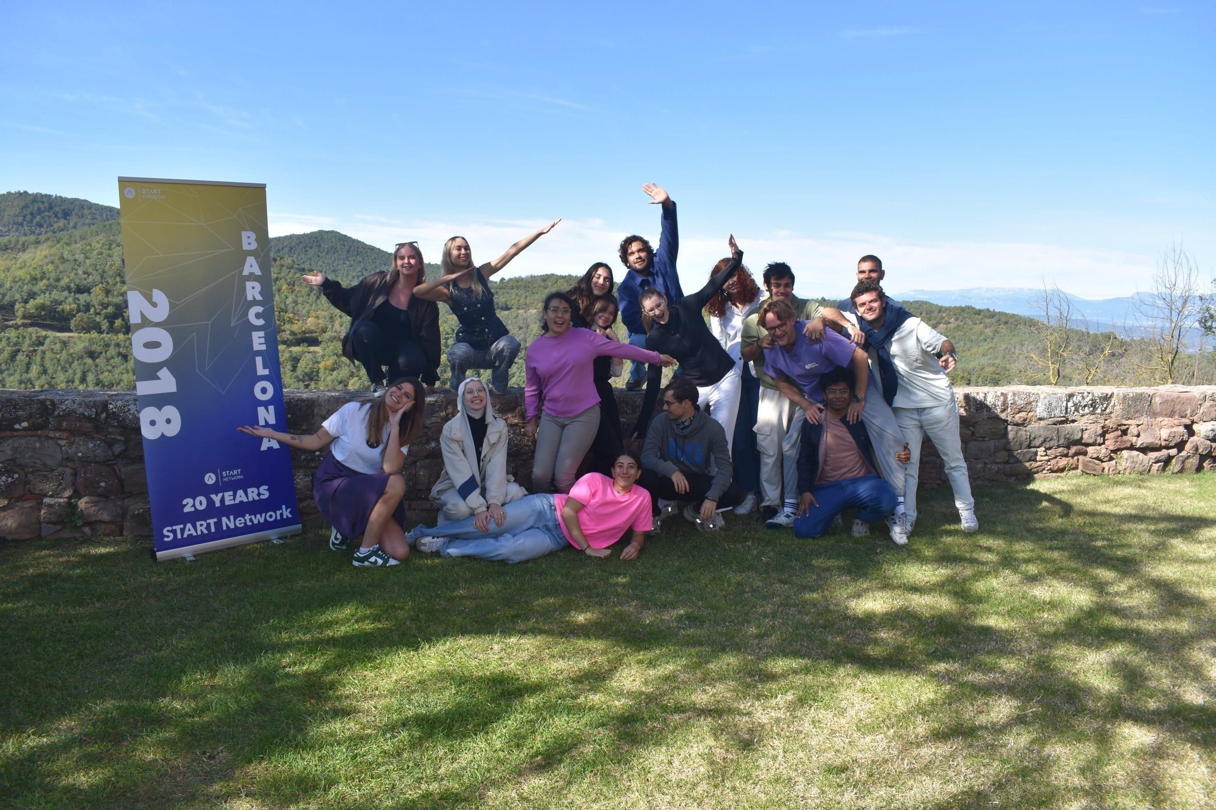 The whole group jumping and posing on a lawn in the hills next to the START Barcelona banner