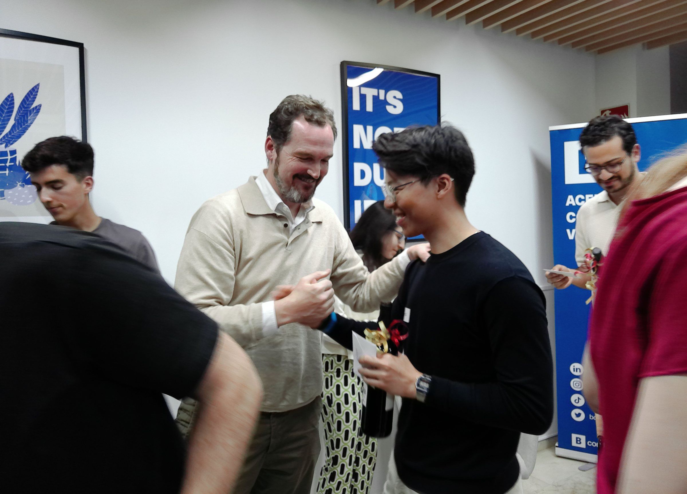 Guests laughing and swapping cards after the investor panel, a bottle of wine in hand