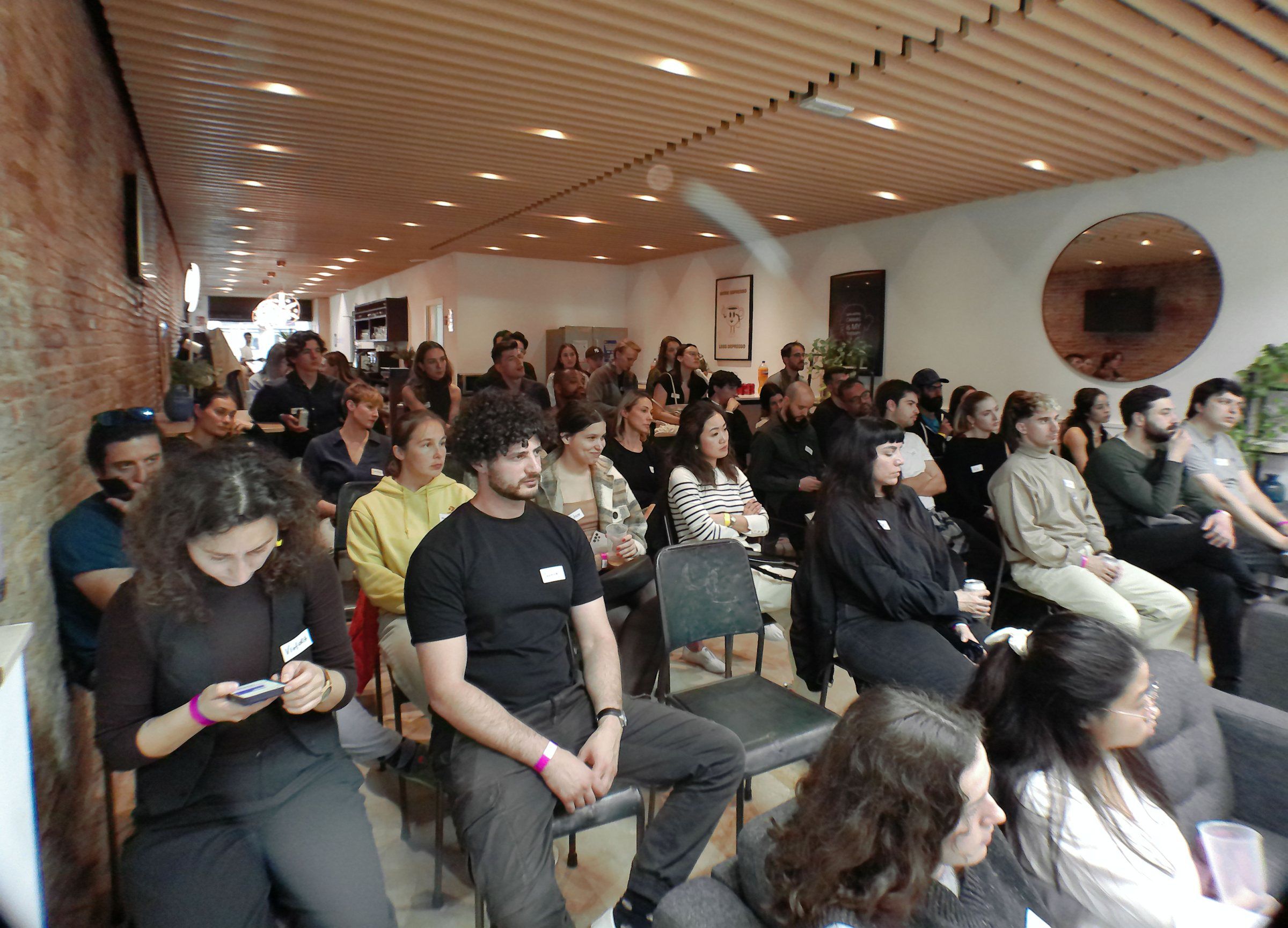 The audience on metal chairs in a brick-walled room, listening to the investor panel